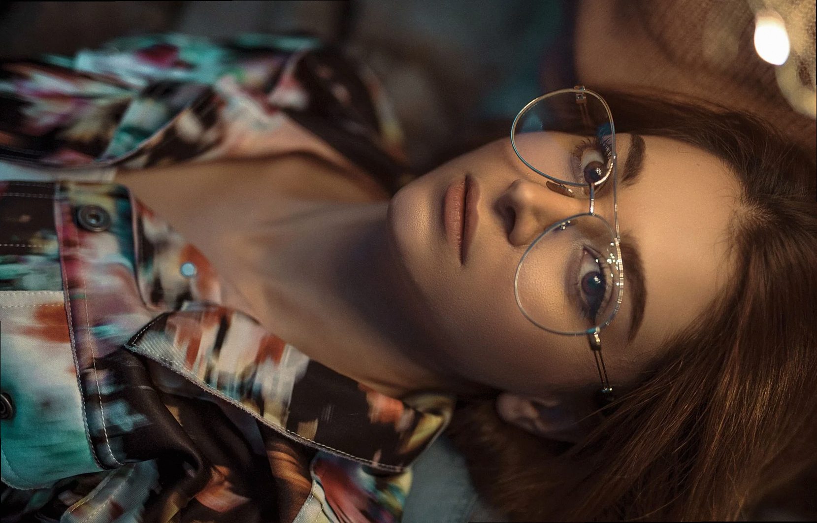 Retrato sereno de una mujer recostada con gafas y chaqueta vibrante.