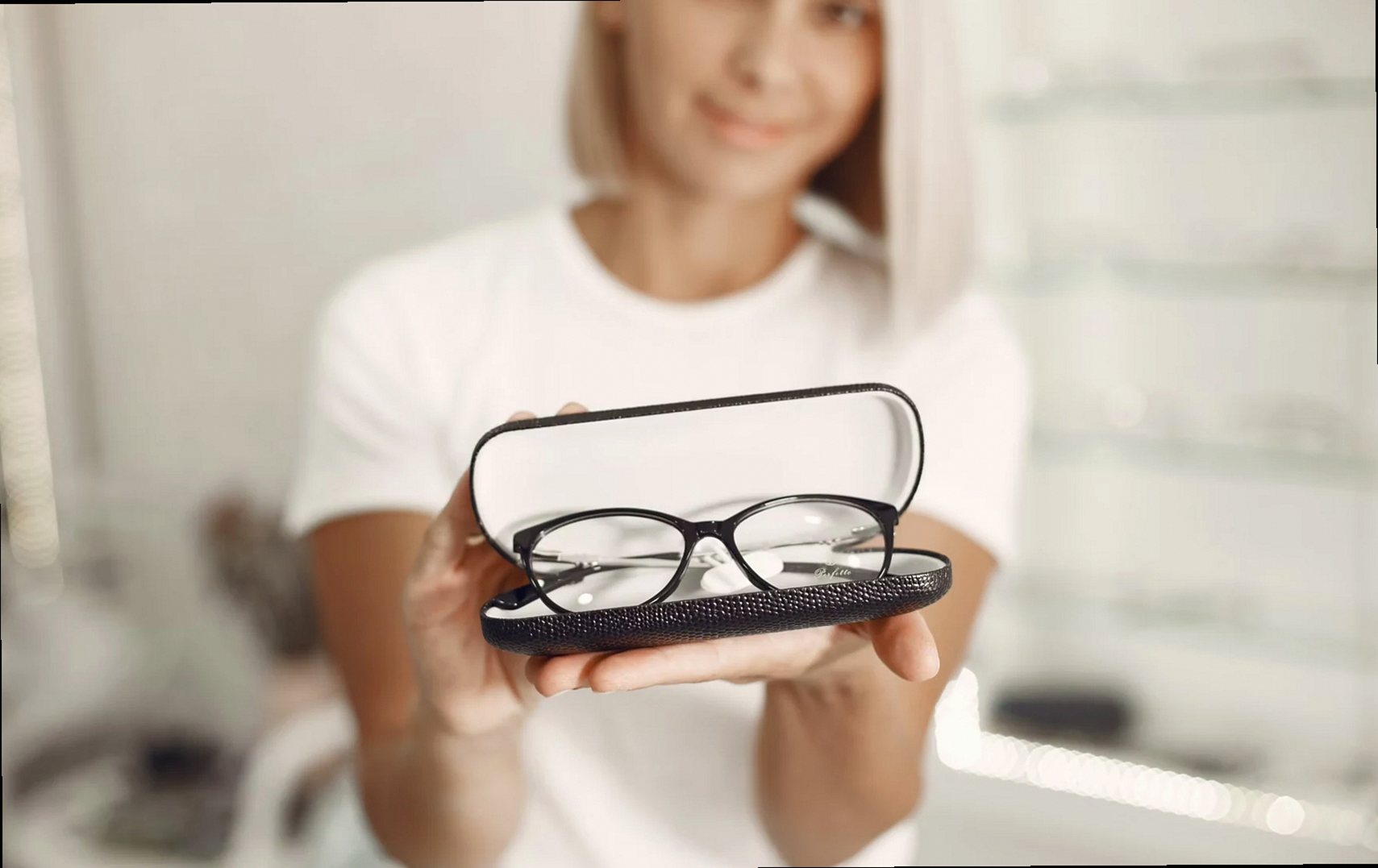 Mujer rubia presentando unas gafas en un elegante estuche en interiores.
