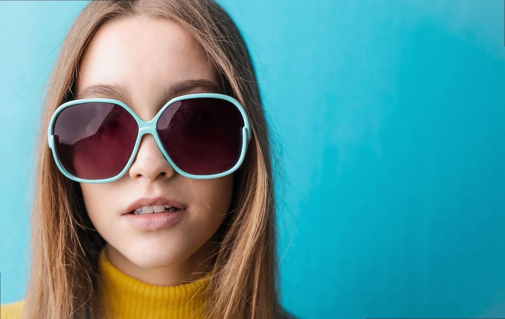 Retrato de moda de una mujer con gafas de sol y suéter amarillo sobre un fondo azul vibrante.